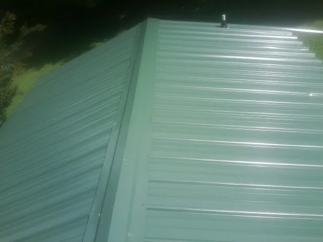 New green metal panels meeting at the ridge of a roof — Flat Roof Repair work by our crew in Byesville