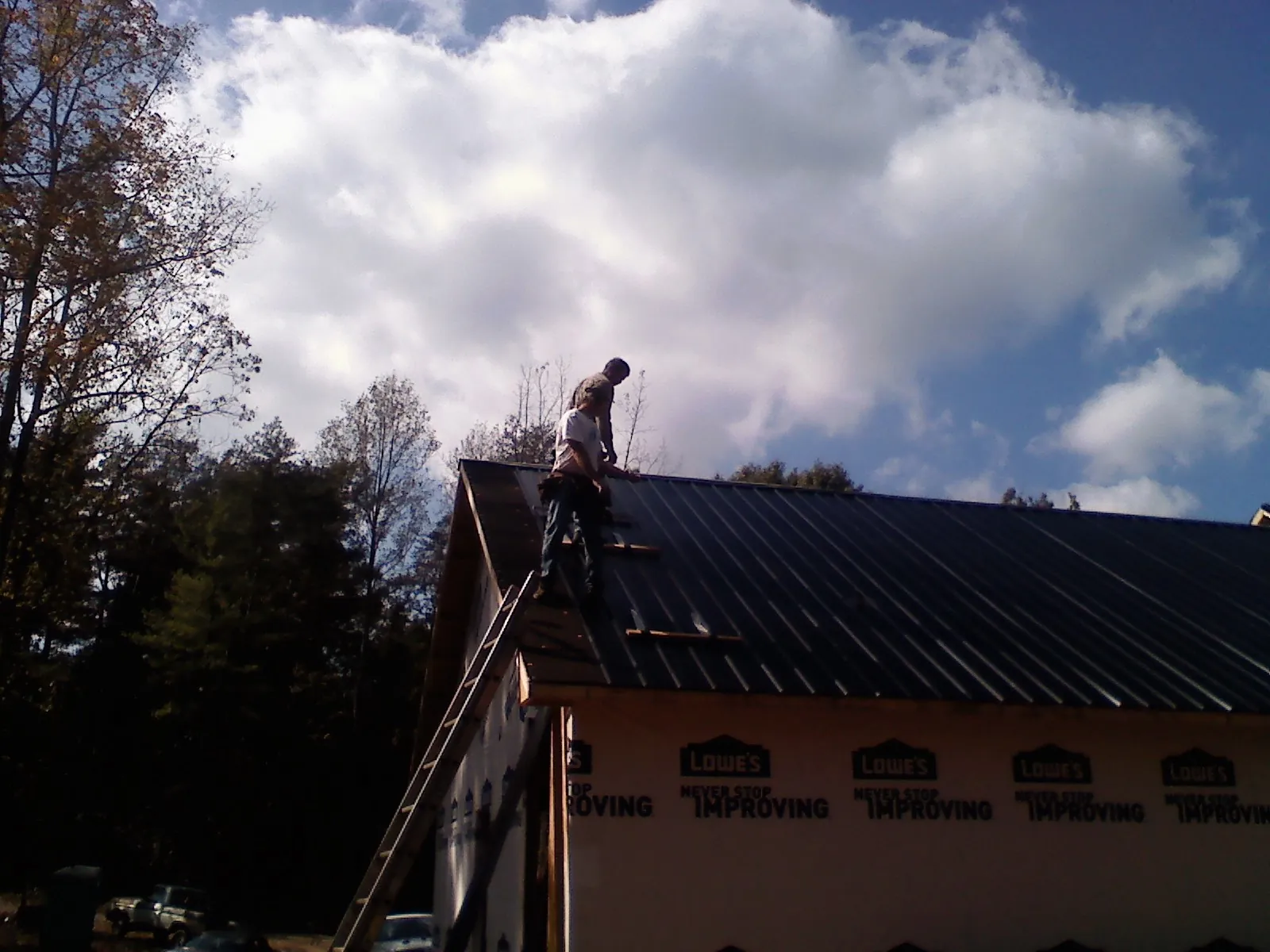Roofer fastening dark metal panels high against a cloudy sky, from a Roof Inspection job in Byesville