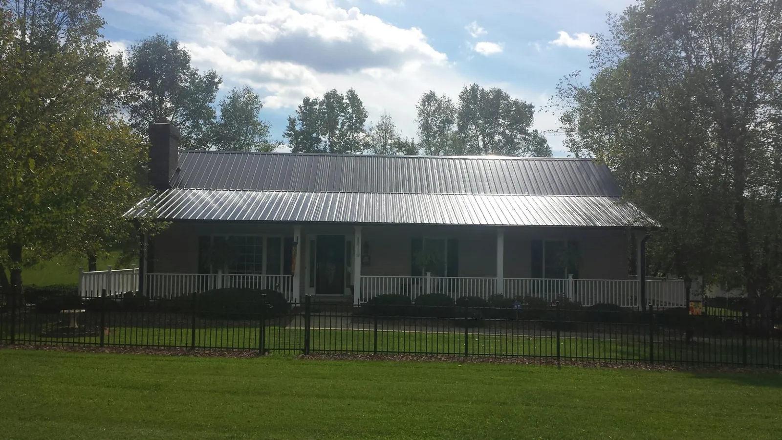 Gray metal roof on a brick ranch with a full width front porch — Gutter Guard Installation work by our crew in Byesville