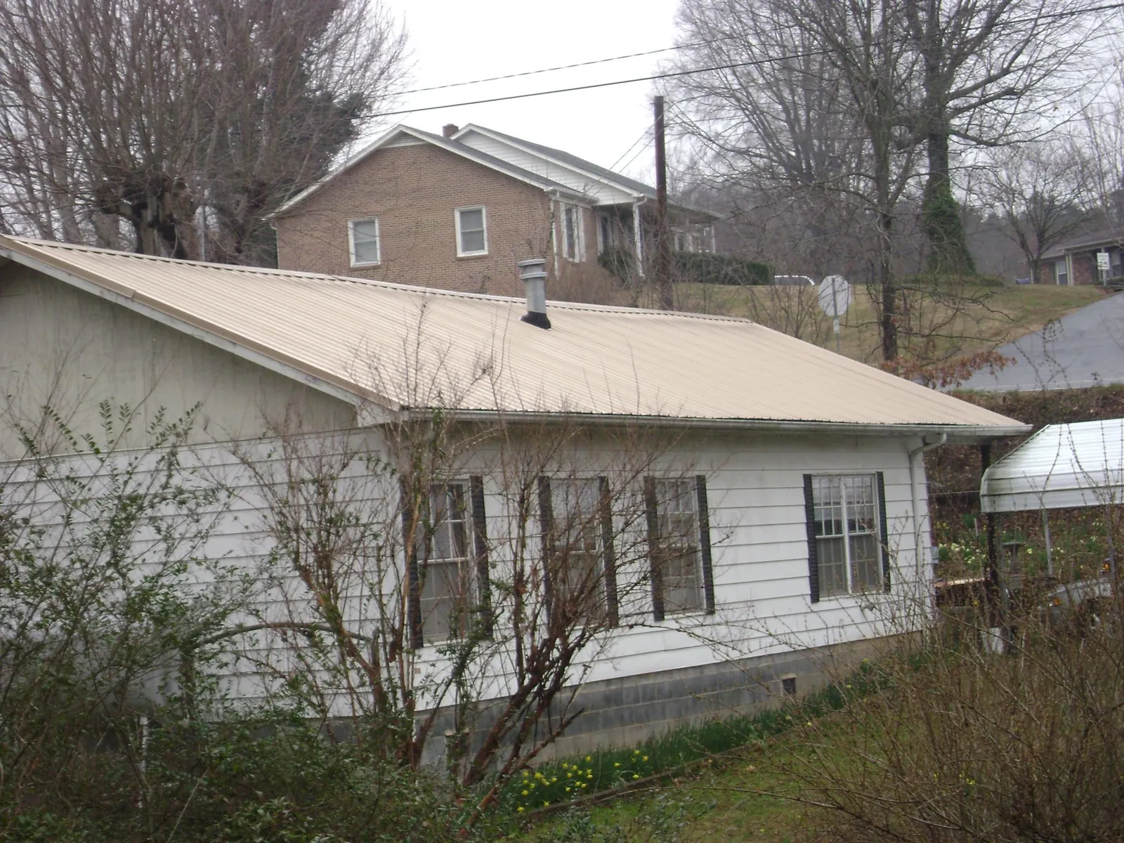 Tan metal roof on a white sided house set into a hillside — Commercial Roofing by Roofing Brothers in Byesville